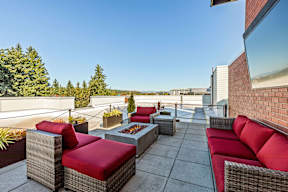 A patio with red cushions and grey wicker furniture.