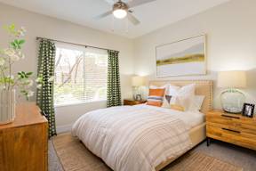 A bedroom with a bed, nightstand, and a painting on the wall.