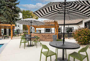 A black and white striped umbrella is over a round table with four chairs.