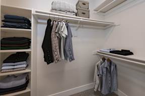 A white closet with clothes hanging and folded on shelves.