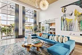 A living room with a blue couch and a large painting on the wall.