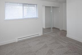 A room with a carpeted floor, a window with blinds, a sliding glass door, and a wall-mounted heater.