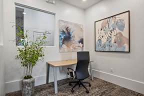 A room with a desk, chair, and two paintings on the wall.