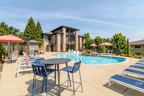 A poolside table with chairs and umbrellas is set up in front of a multi-story building.