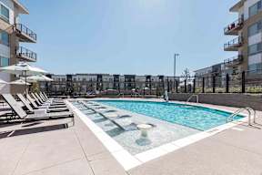a pool with lounge chairs and an apartment building in the background
