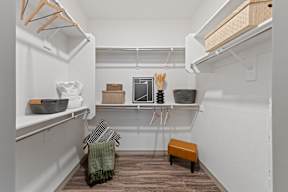 a walk in closet with shelves and baskets and a wooden floor and a white wall