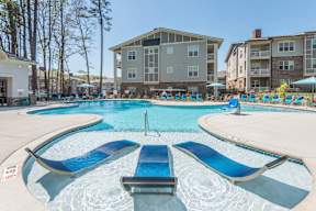 A swimming pool with blue loungers and apartment buildings in the background.