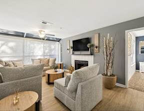 A living room with a grey couch, a white armchair, a wooden coffee table, and a fireplace.