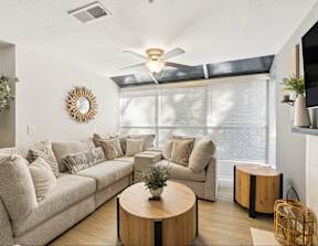 A living room with a beige couch, a round wooden coffee table, and a ceiling fan.
