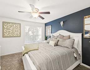 A bedroom with a bed, a ceiling fan, and a painting on the wall.