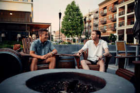 Two men are sitting by a fire pit on a patio.