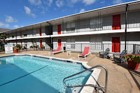 A pool area with red chairs and a white building in the background.