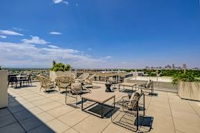 A rooftop patio with chairs and tables overlooking a city skyline.