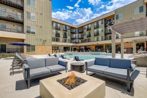 a patio with couches and a fire pit with a pool in the background
