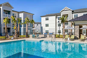 A swimming pool in front of a building with palm trees.