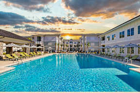 A large swimming pool surrounded by lounge chairs and buildings in the background.
