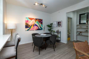 a dining area with a table and chairs and a colorful painting on the wall