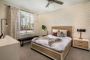 A bedroom with a large bed, a ceiling fan, and a window with blinds.