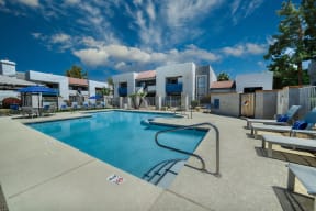 a swimming pool with lounge chairs and umbrellas at the whispering winds apartments in pearland