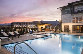 a swimming pool at dusk with a building and mountains in the background