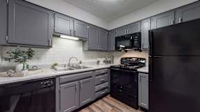 A kitchen with black appliances and grey cabinets.