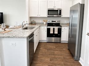 A kitchen with a stainless steel refrigerator, a microwave above the stove, and a sink with a granite countertop.