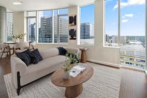 A living room with a couch, coffee table, and large windows overlooking a cityscape.
