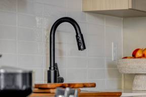 A kitchen sink with a black faucet and a bowl of fruit on the counter.