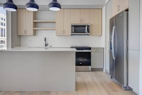 A kitchen with a refrigerator on the right and a stove and microwave on the counter.