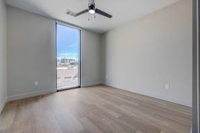 A room with a ceiling fan and a view of the city through a sliding glass door.