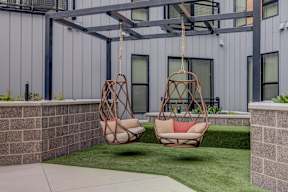 Two hanging chairs are suspended from a metal frame in a backyard.