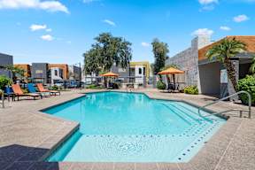 A large swimming pool surrounded by a concrete patio and lounge chairs.