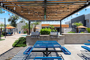 A patio with blue tables and chairs under a wooden roof.