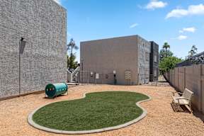 A green barrel sits on a grassy area in front of a grey building.