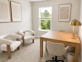A room with a desk, chairs and pictures on the wall.