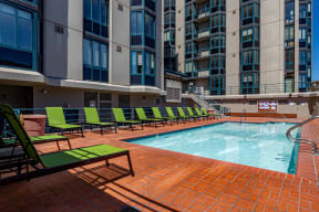 a swimming pool with green lounge chairs and a large building in the background