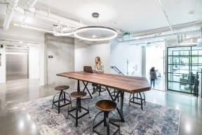 a large wooden table with four stools and a woman working on a laptop in the background
