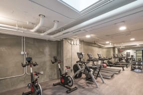 a row of exercise bikes in a room with concrete walls and a skylight