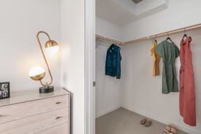 a closet with clothes hanging on a rack and a dresser with a lamp