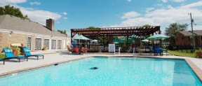 a swimming pool with a patio with chairs and umbrellas