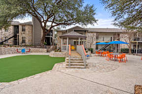 A playground area with a slide and seating area in front of apartment buildings.