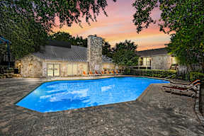A swimming pool surrounded by trees and a house in the background.