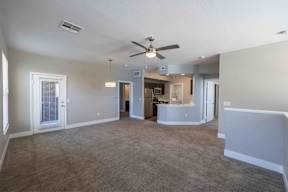 A spacious living room with a ceiling fan and a kitchen area in the background.