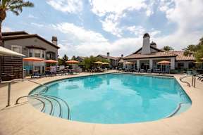 A large swimming pool in front of a building with a patio and umbrellas.