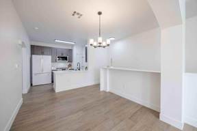 A kitchen with a white fridge and a white island with a chandelier hanging from the ceiling.