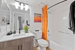 A bathroom with a white toilet, sink, and orange curtain.