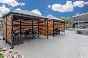 A wooden structure with a black roof and a table and chairs in front of it.