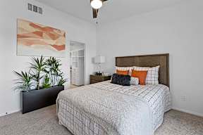A bedroom with a bed, nightstand, and a plant.
