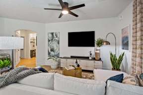 A living room with a white couch and a flat screen TV mounted on the wall.