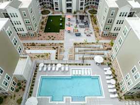 A large swimming pool is surrounded by white lounge chairs and umbrellas.